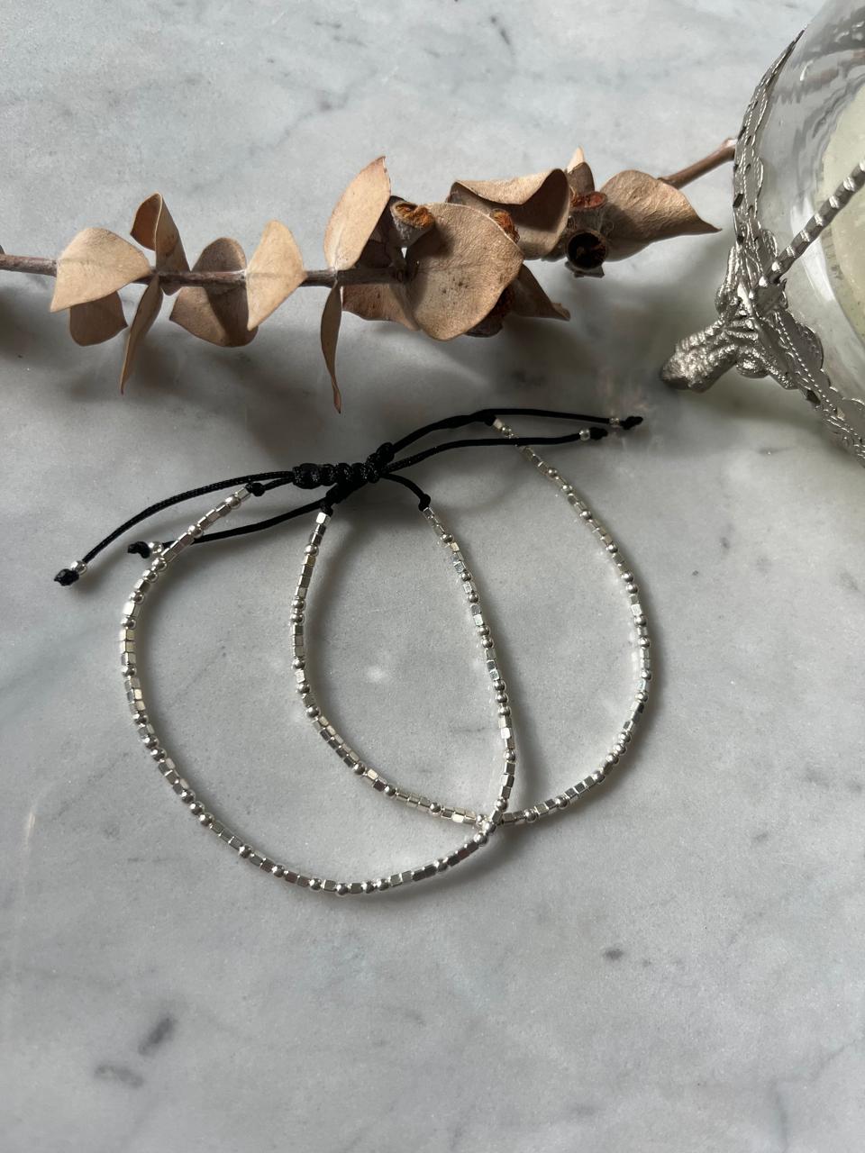 Pulsera ajustable de hilo negro con mostacillas de plata.