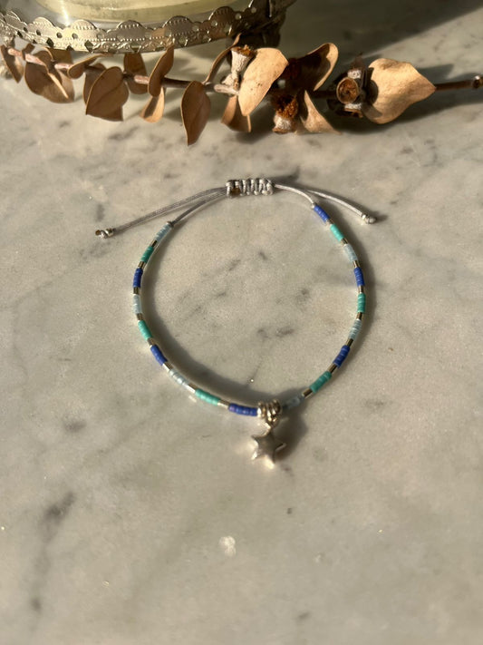 Pulsera de hilo gris, con cristales de colores celestes azules, mostacillas de plata y estrella en plata