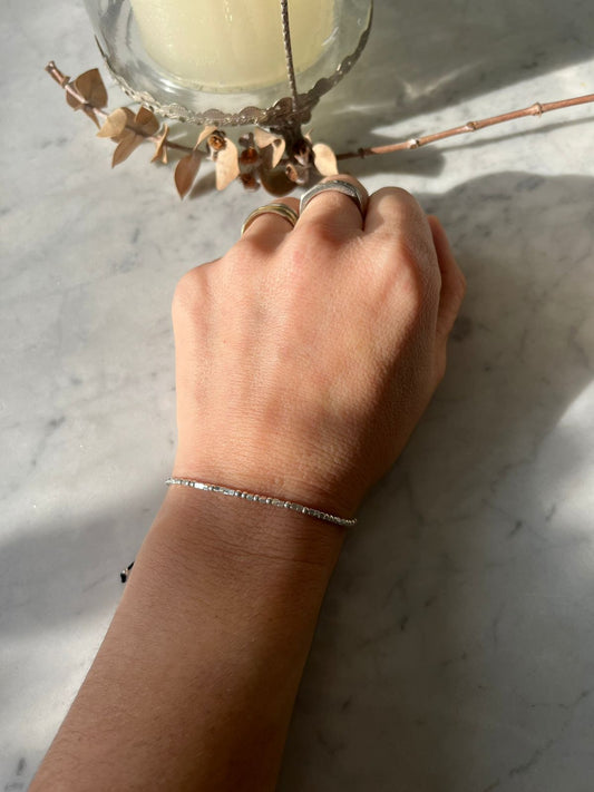 Pulsera ajustable de hilo negro con mostacillas de plata.