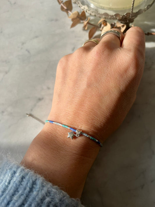 Pulsera de hilo gris, con cristales de colores celestes azules, mostacillas de plata y estrella en plata